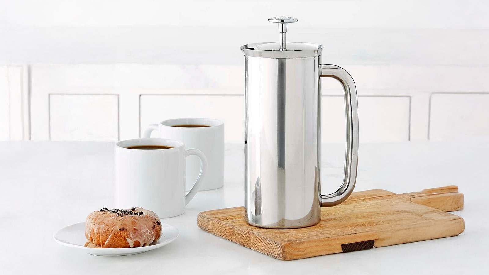 Stainless steel French press on a wooden board with two coffee mugs for Best Coffee Gifts for 2025.