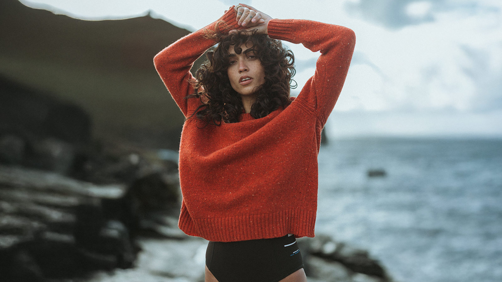 Chunky orange knit sweater worn by the sea, a cozy winter staple and one of the best holiday gifts for women