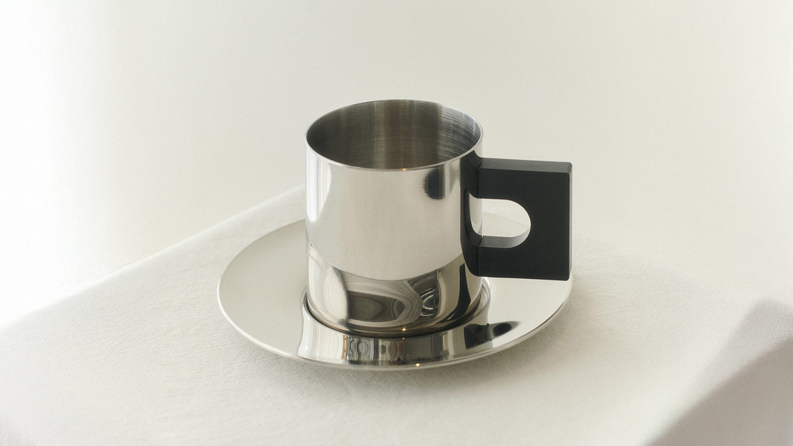 Minimalist stainless‑steel cup and saucer with modern geometric handle — refined gifts for design lovers.