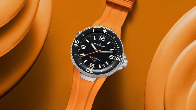 Blancpain Fifty Fathoms Tech 5029 dive watch with brushed titanium case, black dial, ceramic bezel, and bold orange rubber strap—combining professional diving specs with refined lifestyle appeal.