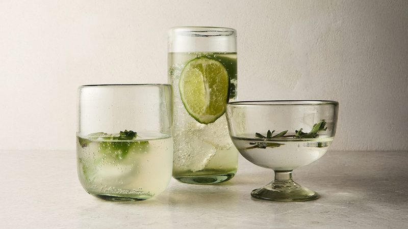 Three glasses with water and limes against a gray background