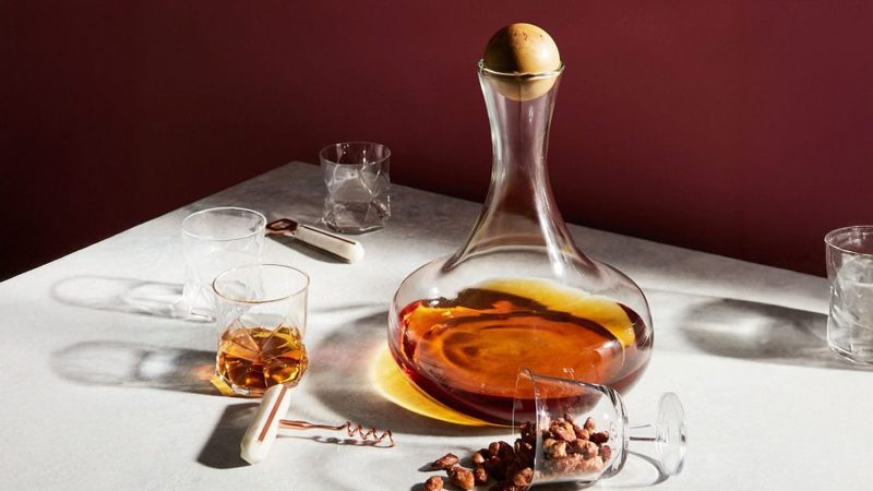 A decanter and glasses on a table against a maroon background