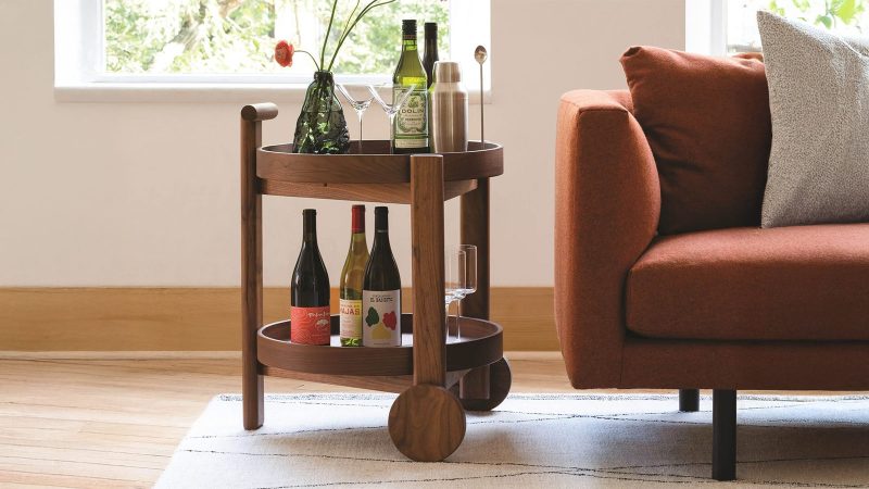 A modern wooden bar cart with bottles next to. n orange couch
