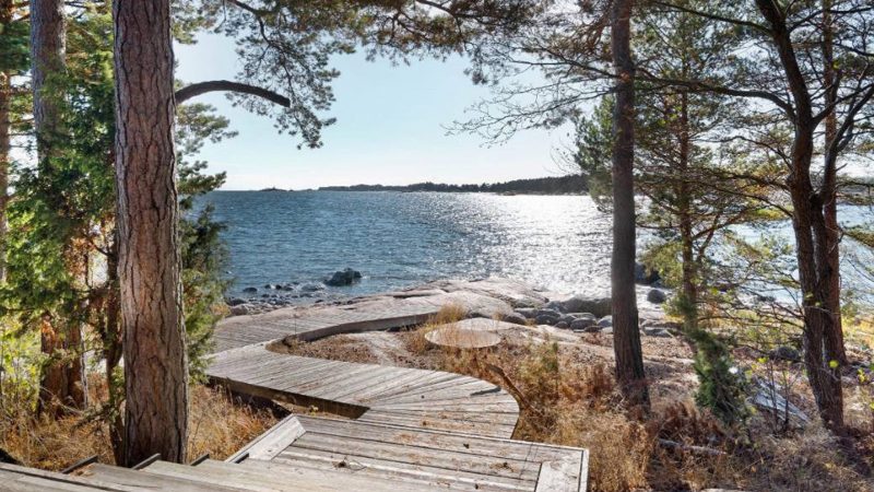 Scandinavian-off‑grid island retreat: Corten-steel homes, sauna, sunken terrace, nestled pine & rugged Baltic shoreline.