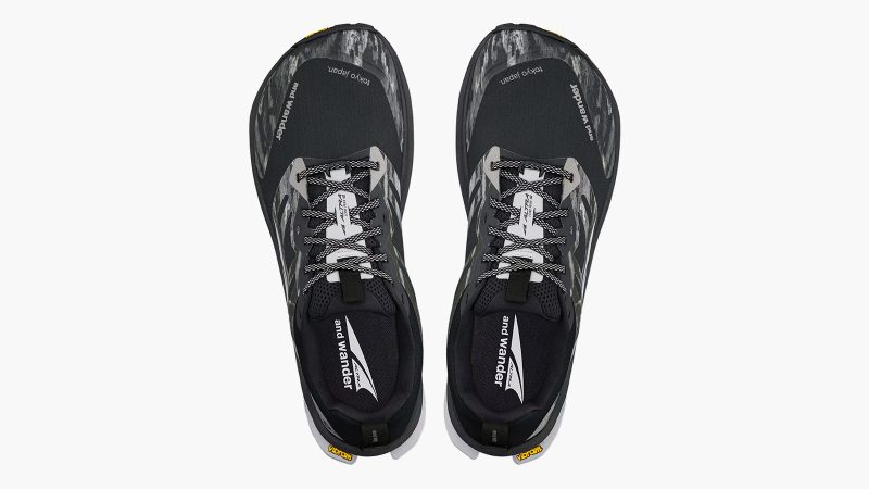 Altra x and wander Lone Peak 9+ trail shoe with alpine graphic overlays, Vibram Megagrip outsole, zero-drop platform, and bold orange and black colorways.