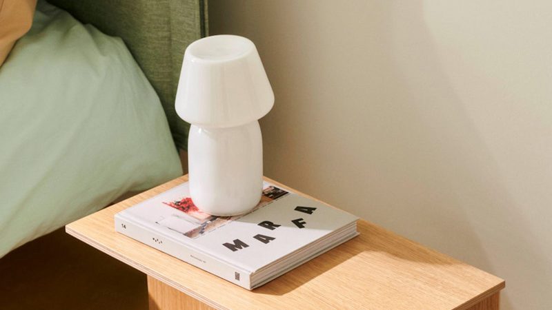 White glass Hay lamp on a bedside table with books – soft lighting with modern design for men’s home essentials.