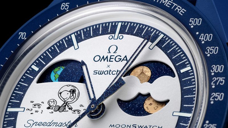 Omega x Swatch Mission to Earthphase Moonshine Gold watch with navy Bioceramic case, Moonshine Gold moon indicators, and UV-reactive Snoopy art.