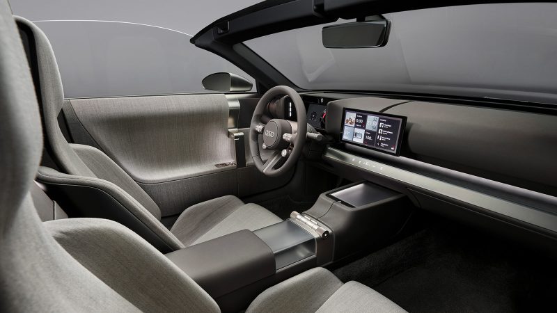 The Audi Concept C is an all-electric two-seat roadster featuring a vertical frame grille, a titanium finish, and a retractable hardtop, showcasing Audi’s next-generation design.