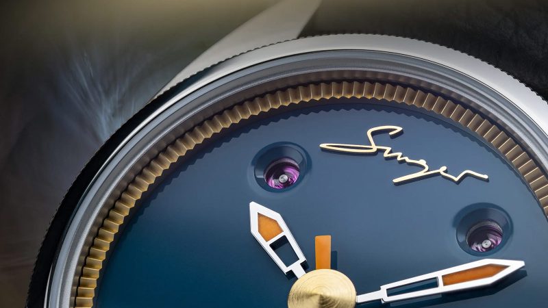 The Singer Caballero watch with stainless steel C-shaped case, green, black, or blue lacquered dial, inset rubies, and signature orange-lumed hands on a textile or leather strap.