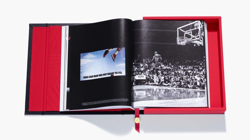 A deluxe edition book titled ‘Air Jordan: The Ultimate Collection’ by Assouline, encased in an ornate black leather clamshell box embossed with Baroque motifs, with a red ribbon and gold medallion bookmark visible.