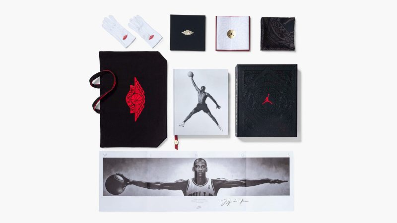A deluxe edition book titled ‘Air Jordan: The Ultimate Collection’ by Assouline, encased in an ornate black leather clamshell box embossed with Baroque motifs, with a red ribbon and gold medallion bookmark visible.