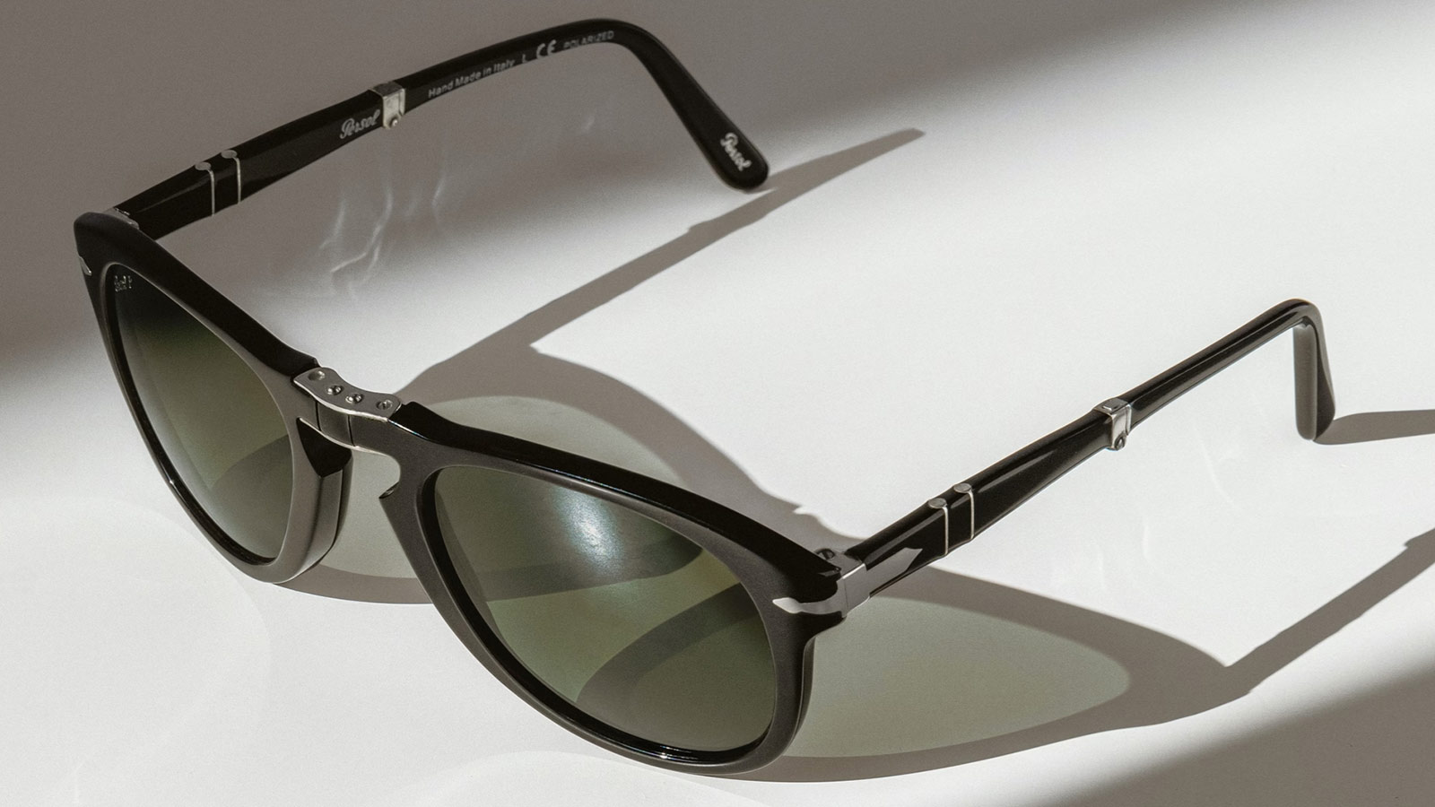 Foldable black Persol 714 sunglasses with green lenses, ideal for fall transitions from trail to town.
