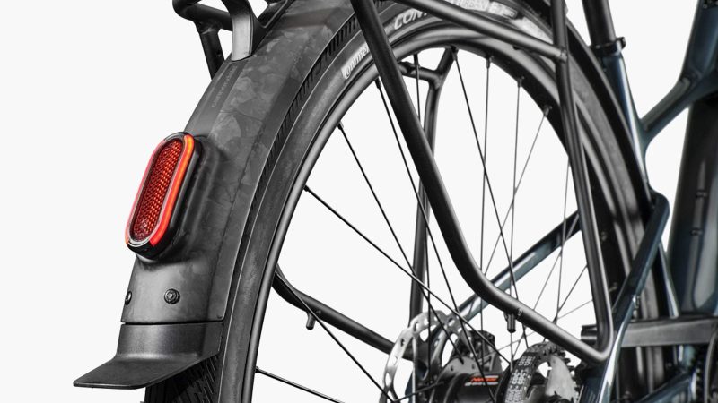 The Cannondale FlyingV carbon e-bike with V-frame design, carbon fenders, and belt-drive system displayed in an urban setting.