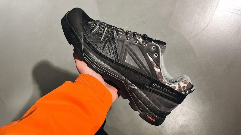 The Carhartt WIP x Salomon X-ALP is a black leather and synthetic trail sneaker with duck camo collar, rubber mudguard, and Utilitarian workwear flair.
