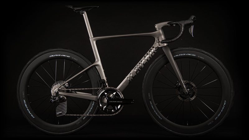 A sleek matte-titanium J.Laverack Speedform road bike with 3-D printed frame sections, internal cable routing, and aerodynamic tubing against a dark studio background.