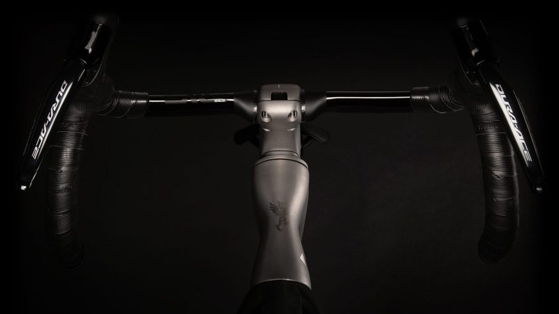 A sleek matte-titanium J.Laverack Speedform road bike with 3-D printed frame sections, internal cable routing, and aerodynamic tubing against a dark studio background.