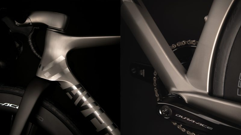 A sleek matte-titanium J.Laverack Speedform road bike with 3-D printed frame sections, internal cable routing, and aerodynamic tubing against a dark studio background.