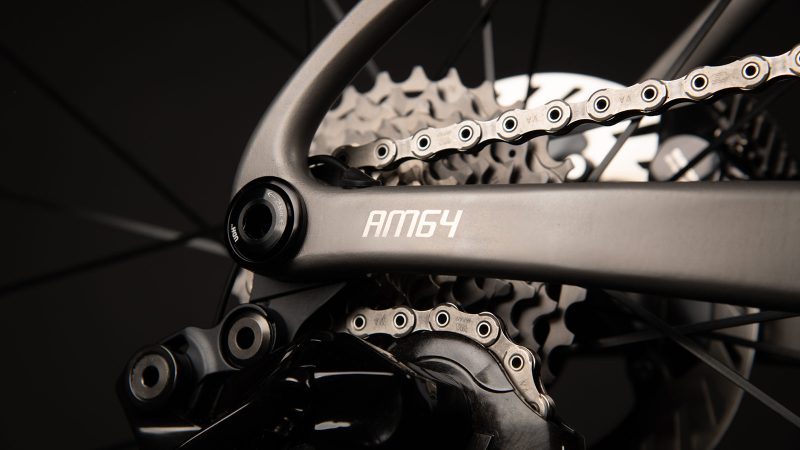 A sleek matte-titanium J.Laverack Speedform road bike with 3-D printed frame sections, internal cable routing, and aerodynamic tubing against a dark studio background.