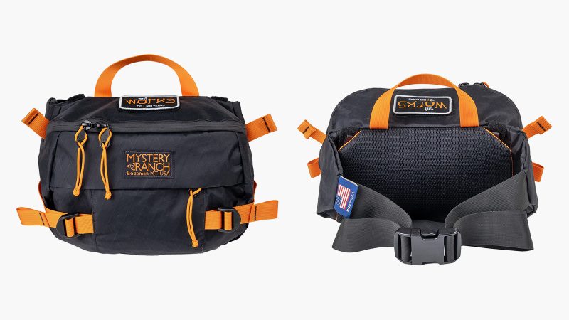 Mystery Ranch Hip Monkey 25 Legacy Edition waist pack in X-Pac sailcloth with orange trim, commemorative patch, and adjustable hip belt.