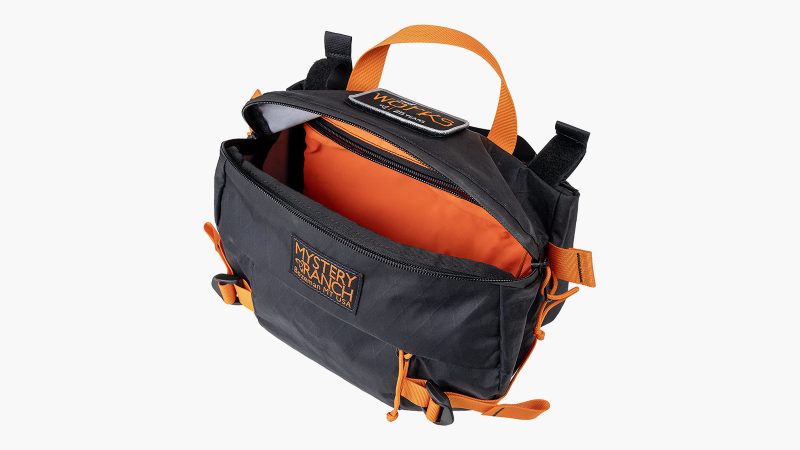 Mystery Ranch Hip Monkey 25 Legacy Edition waist pack in X-Pac sailcloth with orange trim, commemorative patch, and adjustable hip belt.