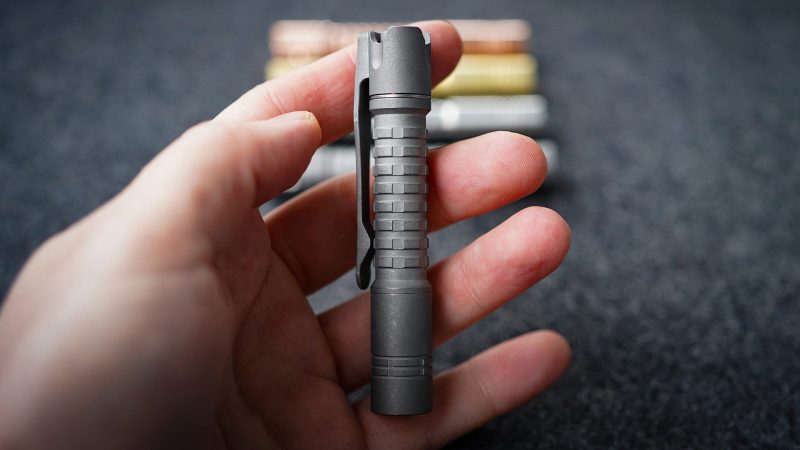 ReyLight Pineapple Mini MKIII Titanium Flashlight featuring a reverse clicky switch, titanium clip, and 4000K Nichia LED, showcased on a dark EDC gear setup.