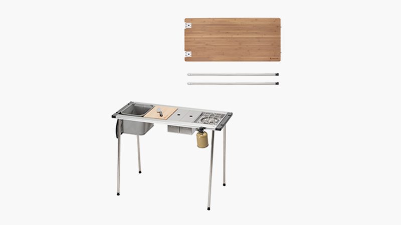 Snow Peak Iron Grill camp kitchen and table setup outdoors features modular stainless steel cooking units and a wooden tabletop for outdoor dining.
