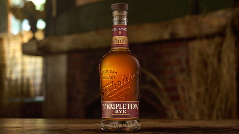 Templeton Single Barrel Rye whiskey features a cask strength release label, set against a rustic distillery backdrop.