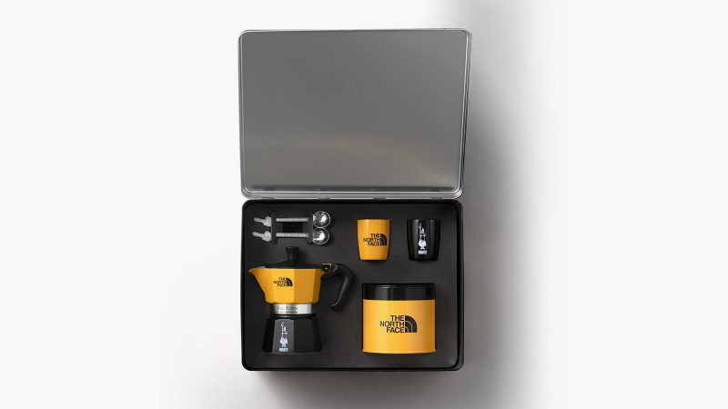The North Face x Bialetti Moka Express Set features a co-branded stovetop espresso maker and camping mug in an outdoor alpine setting, designed for trail-side coffee brewing.