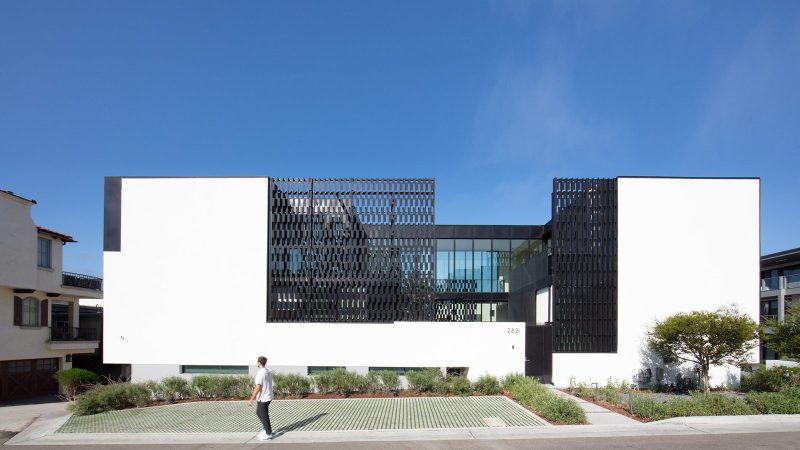 The Alma Switch House in Manhattan Beach features a modern white stucco facade, a shimmering silver aluminum privacy screen, and an open-air central courtyard.
