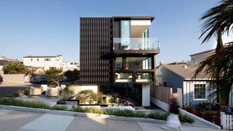 The Alma Switch House in Manhattan Beach features a modern white stucco facade, a shimmering silver aluminum privacy screen, and an open-air central courtyard.
