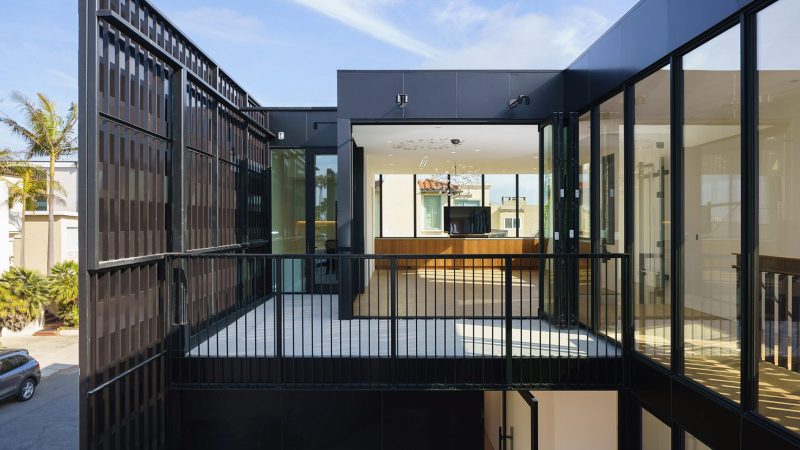 The Alma Switch House in Manhattan Beach features a modern white stucco facade, a shimmering silver aluminum privacy screen, and an open-air central courtyard.