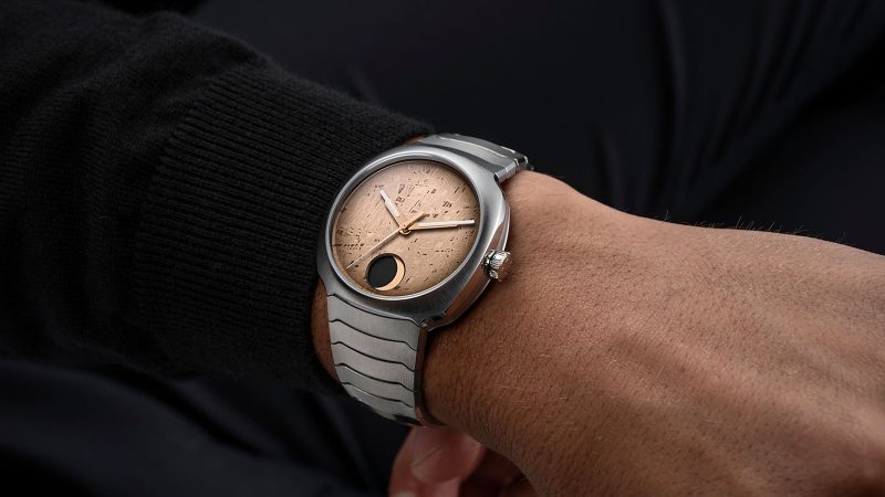 The H. Moser & Cie. Streamliner Perpetual Moon Concept Meteorite watch with a golden Gibeon meteorite dial, steel integrated bracelet, and moon phase at 6 o'clock.