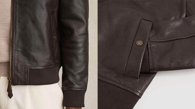 The REISS Cast leather bomber jacket features grained leather, gold-tone hardware, ribbed trims, and a modern minimalist silhouette.