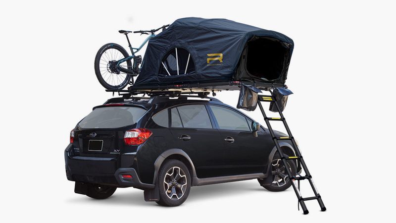 The Roofnest Meadowlark ultralight rooftop tent is mounted on a compact SUV, featuring an open fold-out design with an integrated ladder and foam mattress.