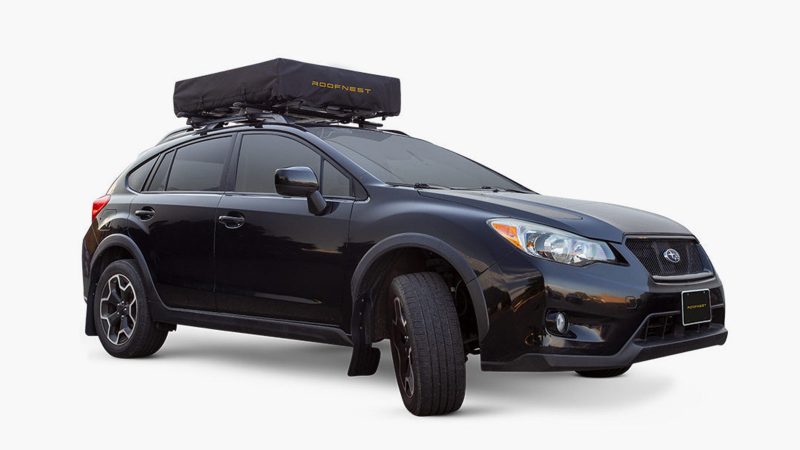 The Roofnest Meadowlark ultralight rooftop tent is mounted on a compact SUV, featuring an open fold-out design with an integrated ladder and foam mattress.