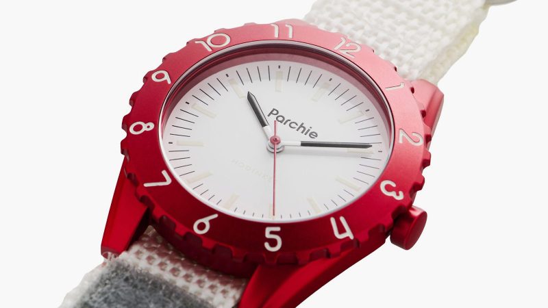 The Parchie Lunar-Time Limited Edition for Hodinkee is a space-inspired watch with a red aluminum case, a white dial, a Velcro strap, and available in 32mm and 36mm sizes.