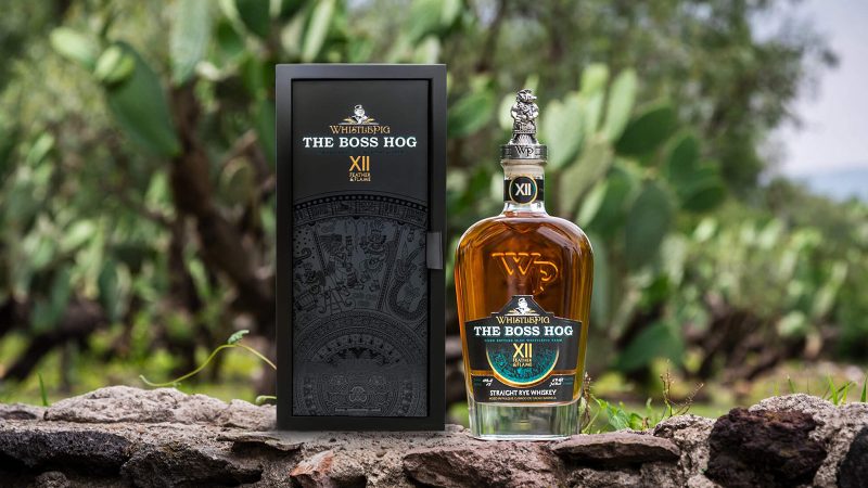 WhistlePig’s The Boss Hog XII Feather & Flame single barrel Rye whiskey bottle with a decorative stopper and a glass of dark amber spirits.